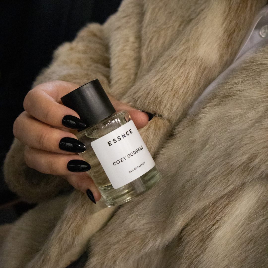 A person with long, black manicured nails holds a bottle of perfume labeled 