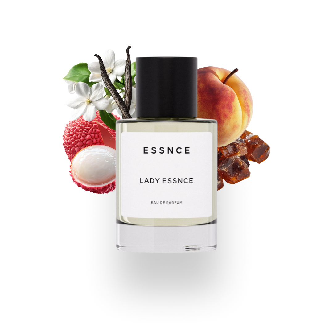 En flaska ESSNCE Lady ESSNCE Eau de Parfum visas med en svart kork och en vit etikett. Bakom flaskan finns ingredienser som litchifrukt, jasmine, patchouli, vanilj, amber och persika.